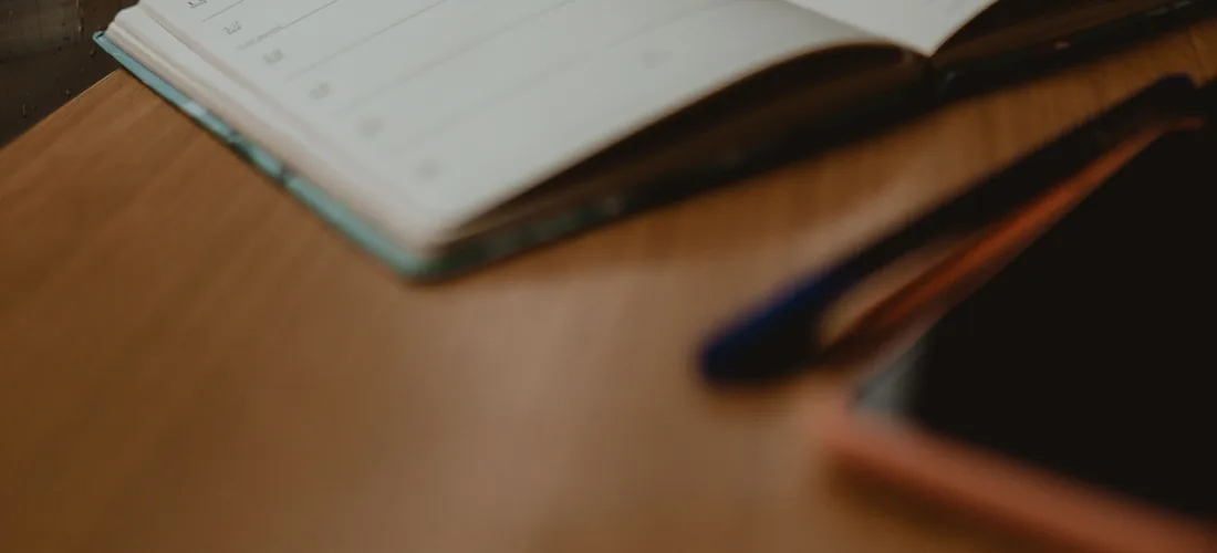 Un cuaderno abierto con una pluma, junto a una ventana con lluvia